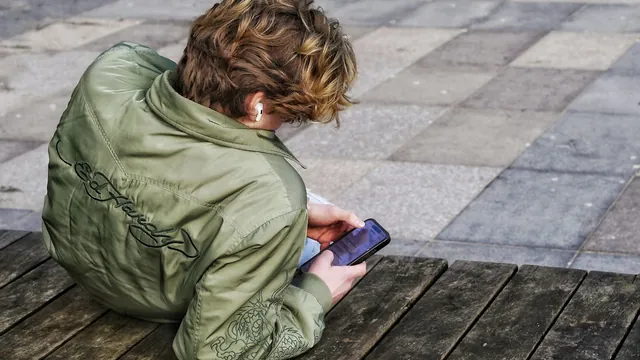 A young person sitting on the ground, looking at a phone