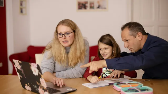 Two parents helping a child at a laptop