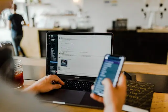 A person at a laptop, reaching for a phone