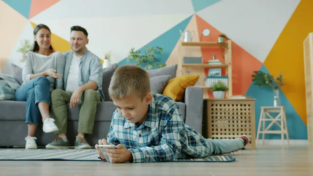 A boy absorbed in a tablet on the floor while his parents watch from the sofa